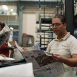 Workers at a newspaper printing press reading freshly printed copies. Focus on a man holding a newspaper. — Anabolics in the