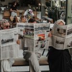 Three adults reading newspapers in a modern Ankara café, enjoying leisure time. — Come i Professionisti Combinano gli Steroid